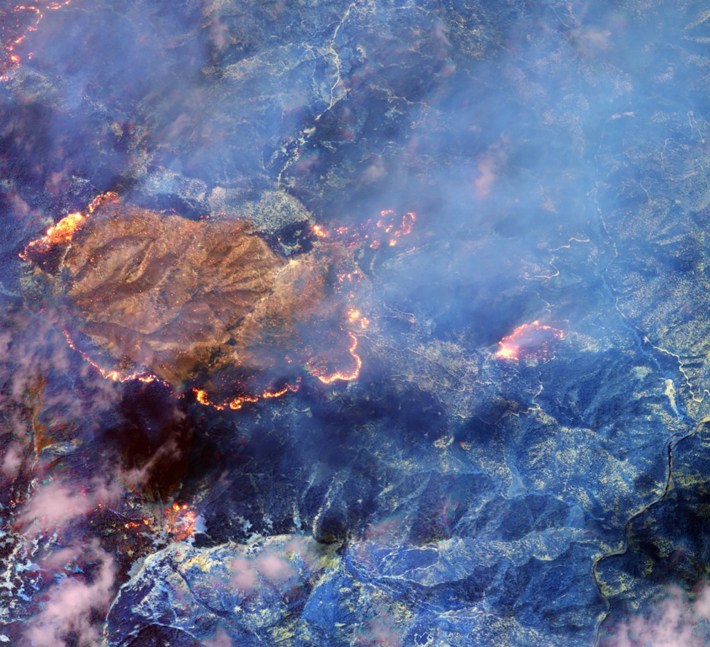 FIGURES 3-4. On August 28, 2014, just 15 days after launch, WorldView-3 captured images of the Happy Camp fire in California’s Klamath National Forest. This is the first example of how WorldView-3 can use its shortwave infrared (SWIR) sensor to see through the dense smoke of an active fire to the ground beneath, and also locate the flame front and hot spots in the fire. The top shot is the same image but it was taken without the SWIR sensor. It’s what you can see in the visible part of the spectrum, which is what a standard commercial imaging satellite would see. In the bottom image with the SWIR sensor, the smoke disappears, and the hot spots in the fire become visible.